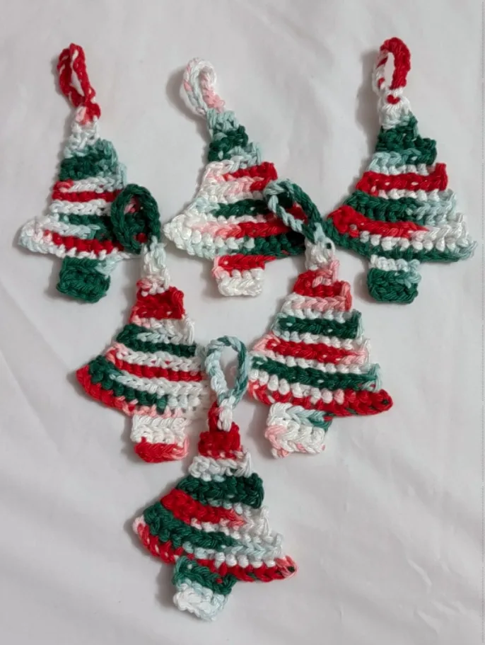 Six hand-crocheted Christmas tree ornaments in red, green, and white stripes lie on a white surface. The text overlay reads…