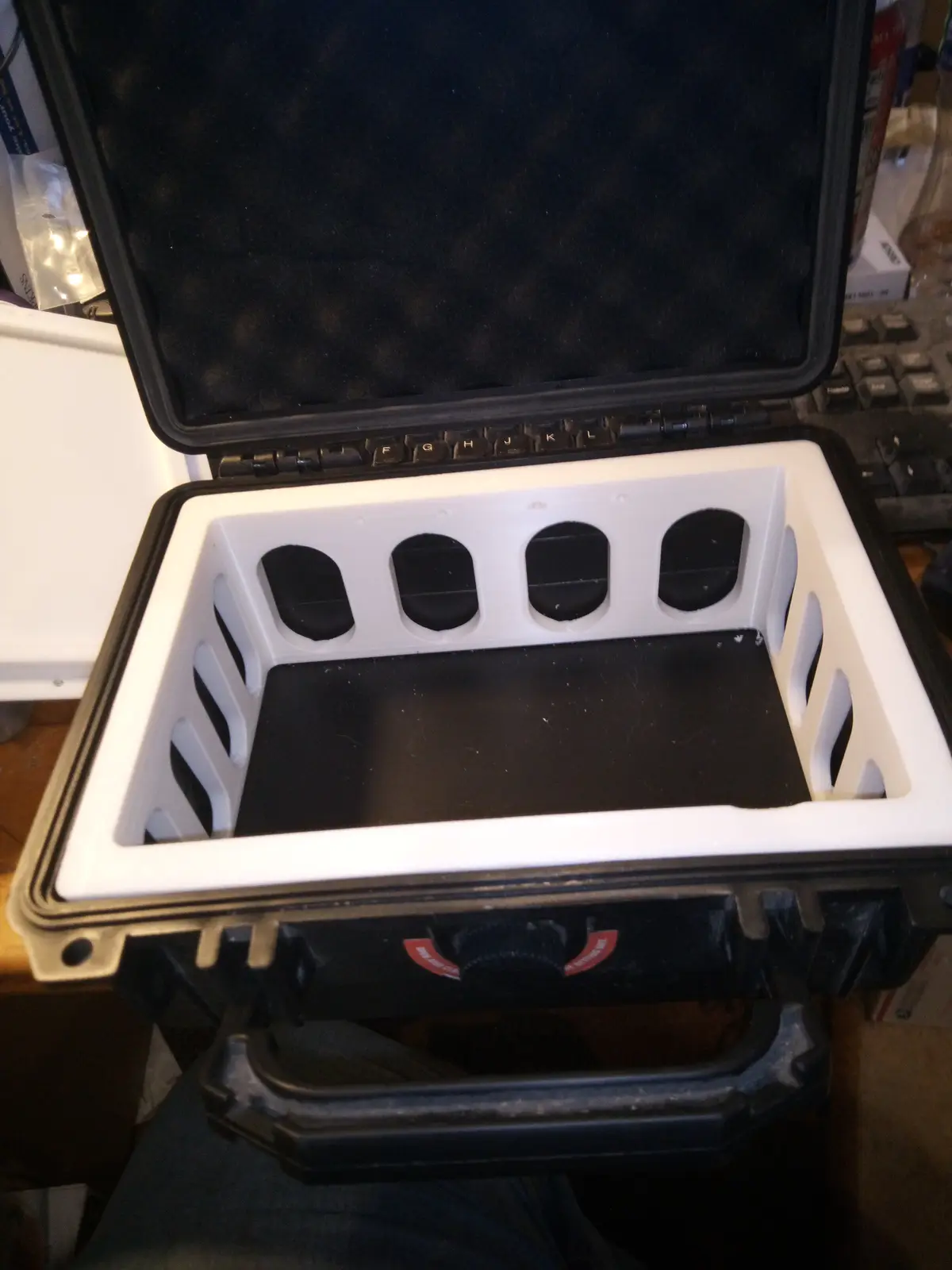 A black hard-shell case is open, revealing a white custom foam insert with four oval cutouts designed to hold keyboard keys…