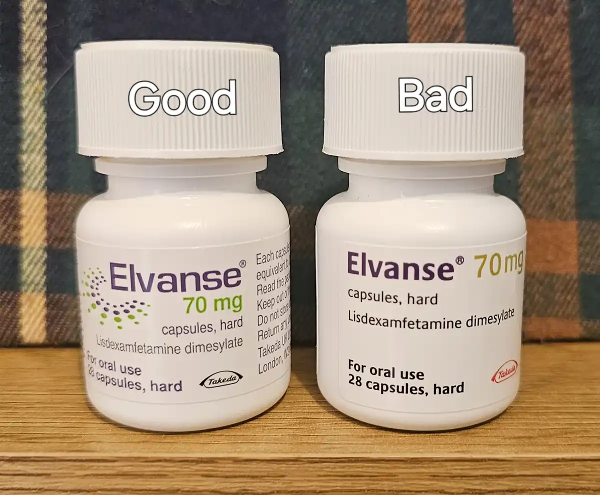 Two identical white bottles of Elvanse 70mg medication sit side-by-side on a wooden surface against a plaid background. The…