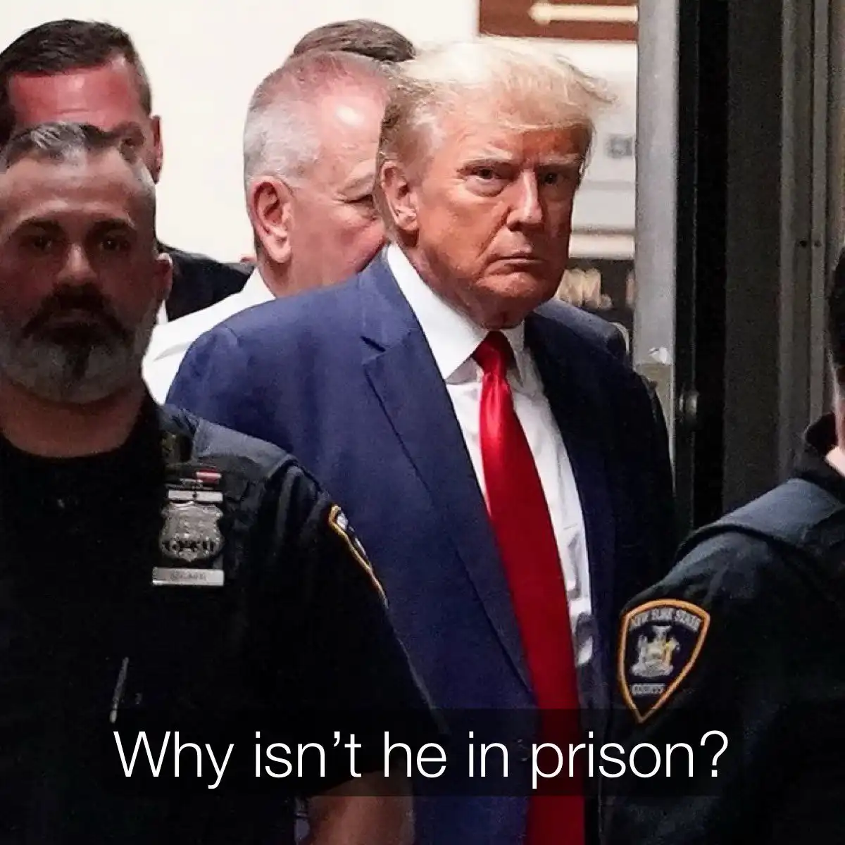 A photo shows Donald Trump in a blue suit and red tie, flanked by New York State Court officers as he walks through a…
