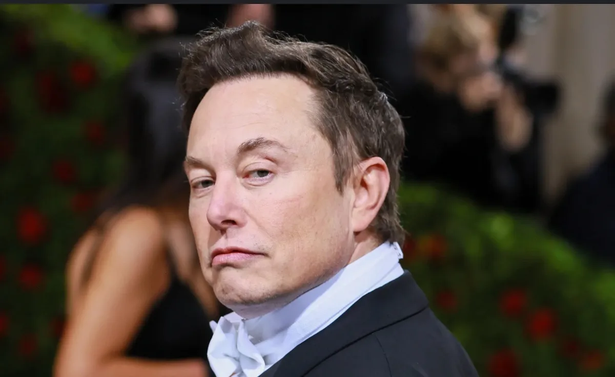 a close-up photo of elon musk in a black tuxedo with a white bow tie, looking slightly to his right with a weary or…