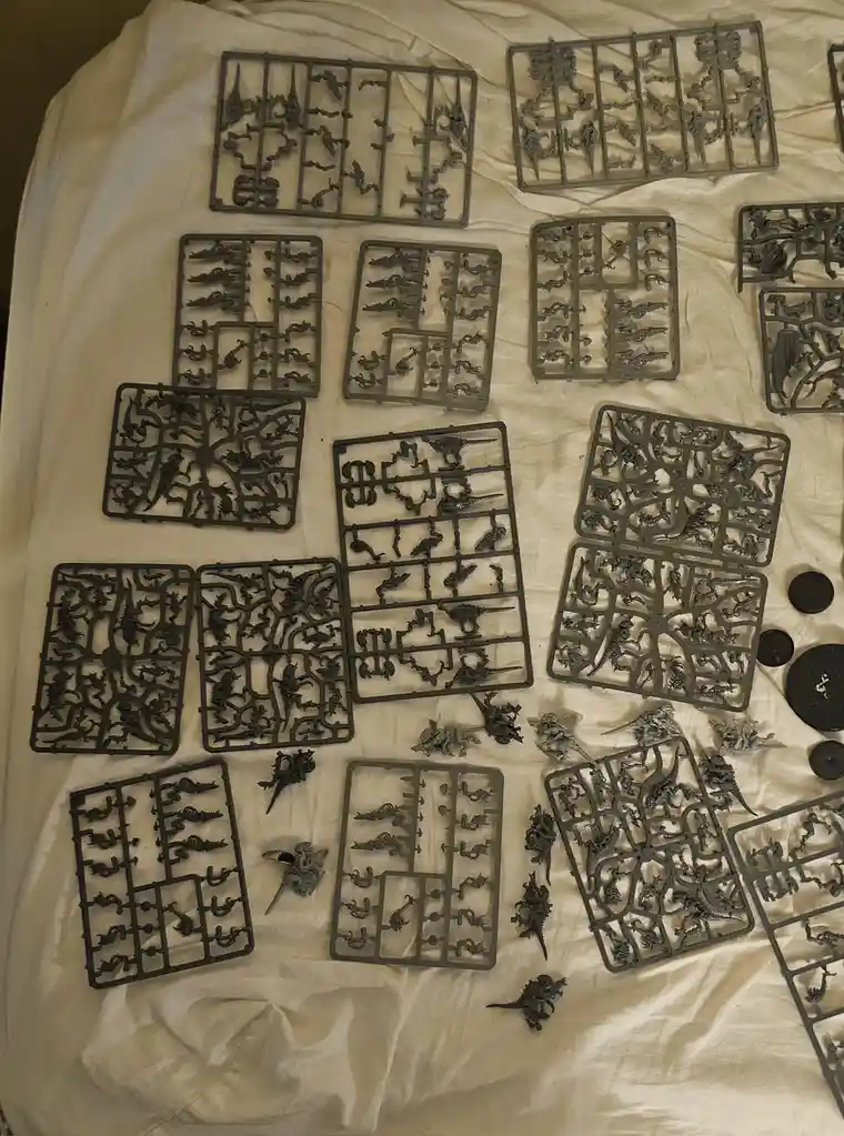 An overhead shot shows numerous grey plastic sprues with intricate fantasy miniatures still attached, scattered across a…