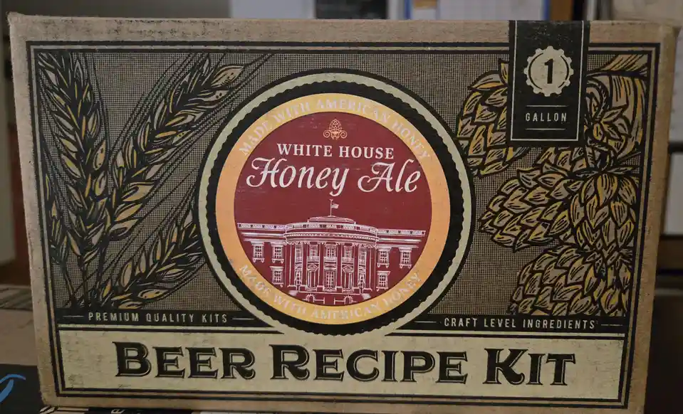 A cardboard box for a beer recipe kit labeled 'White House Honey Ale' features an illustration of the White House building…