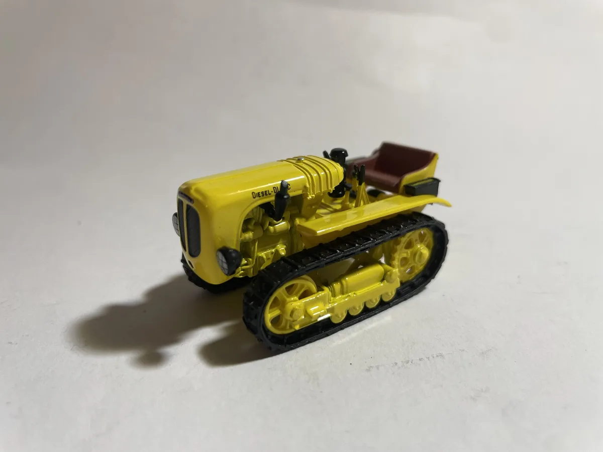 A small yellow toy tractor with black tracks and a red seat sits on a plain white surface, with the text 'diesel-diy'…