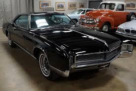 a glossy black classic muscle car with chrome details is prominently displayed in a well-lit indoor car showroom, with other…