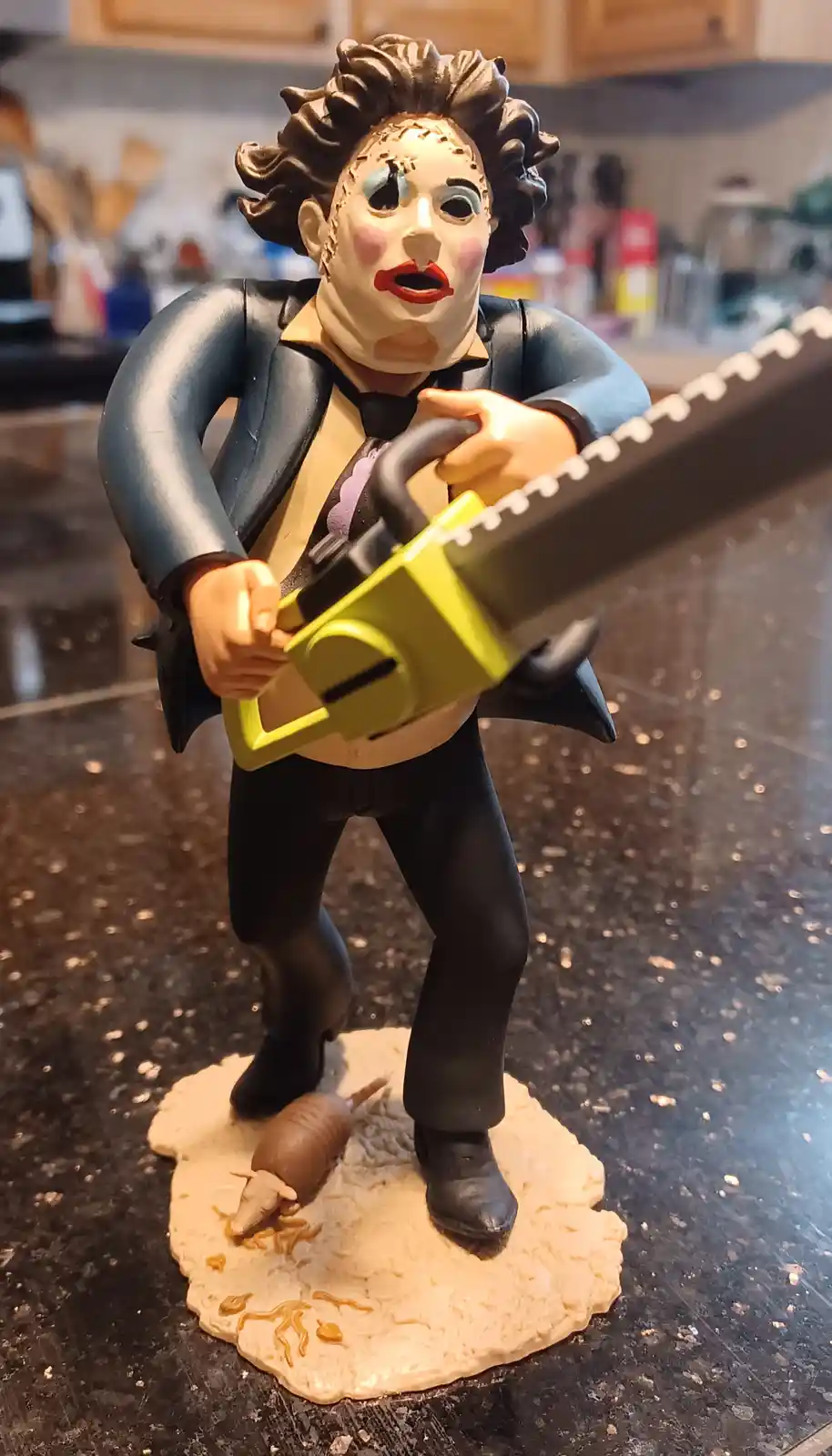 A figurine of the horror movie character Leatherface from 'The Texas Chain Saw Massacre', wearing a suit and holding a…
