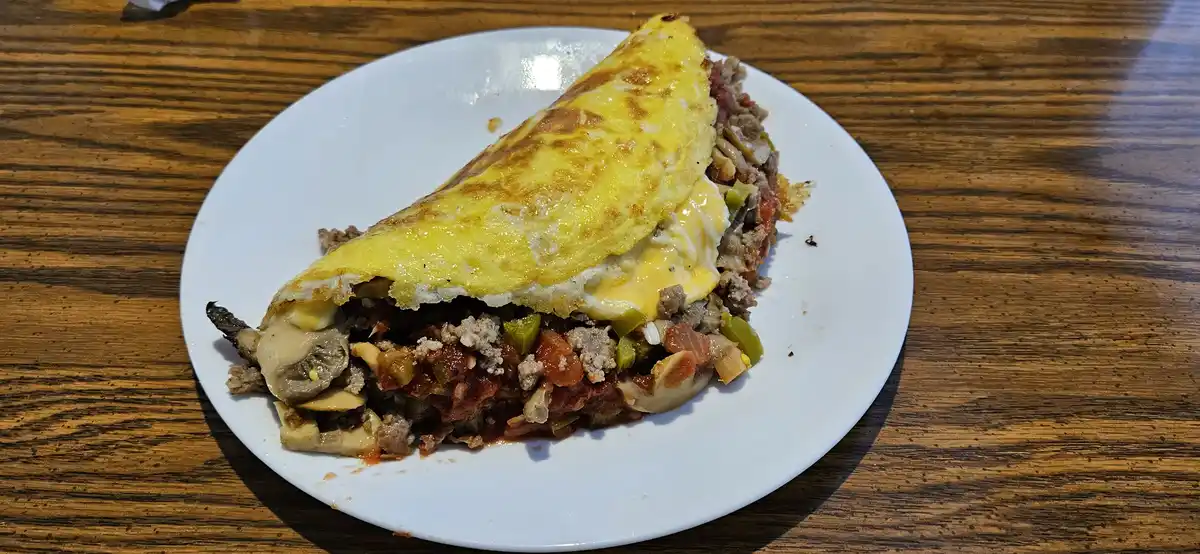 A close-up photo shows a folded, yellow egg dish on a white plate, revealing a filling of ground meat, melted cheese…