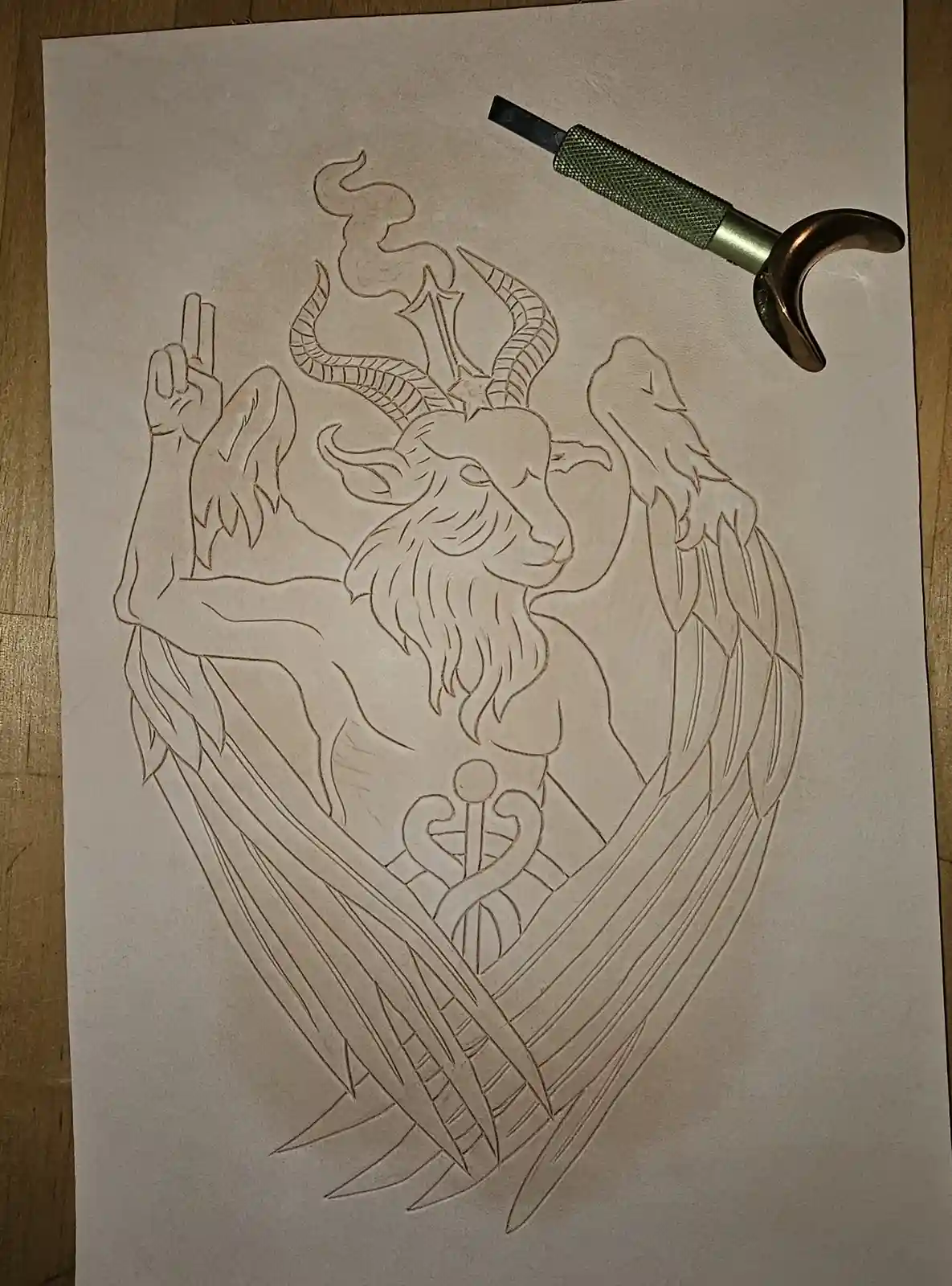 A detailed line drawing on light-colored leather depicts a horned, winged goat-headed figure with a human-like body, holding…