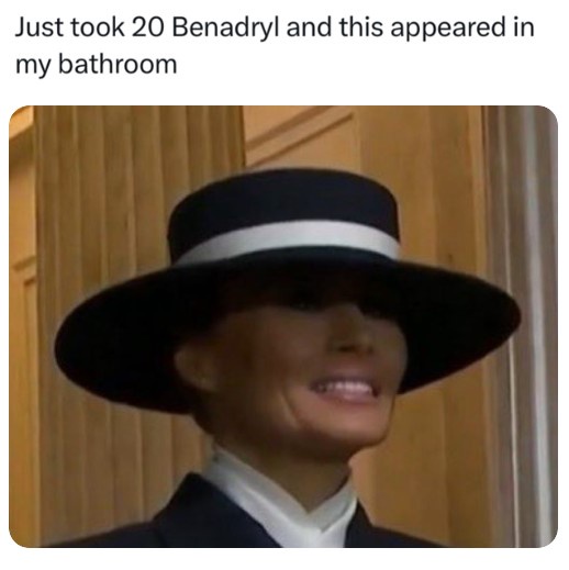 A still image of a woman wearing a black hat with a white band and a dark suit, smiling slightly while looking upward. The…