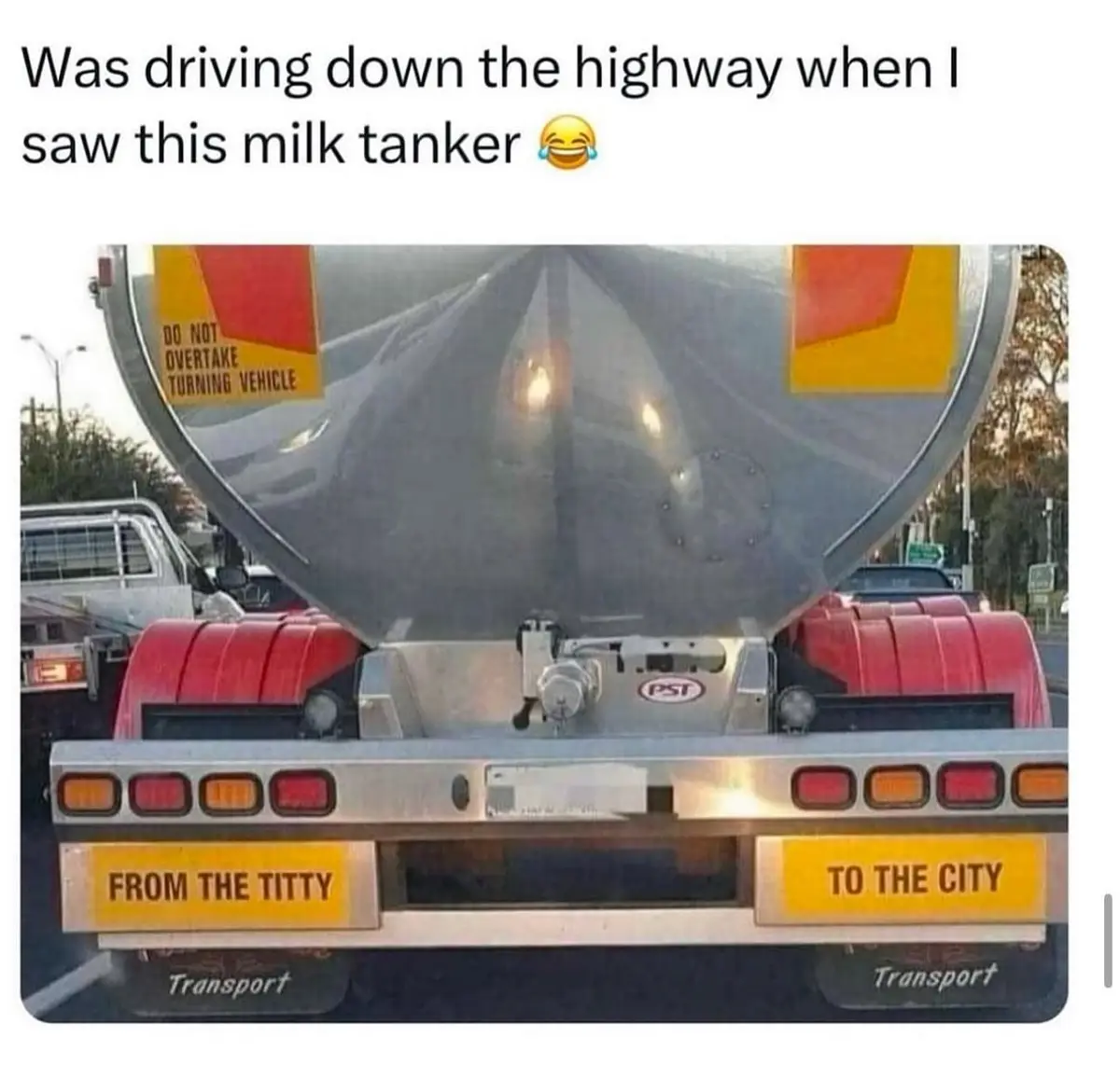 The image shows the rear of a large silver milk tanker truck with red fenders and brake lights. Two yellow signs on the…