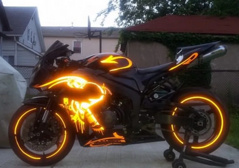 a black sport motorcycle is parked on a driveway, featuring glowing orange flame decals along its body and rims, with a…