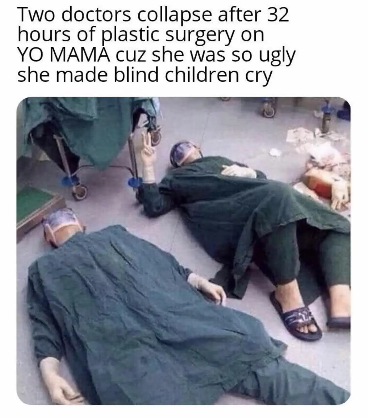 Two people in green surgical scrubs and caps are collapsed on a hospital floor, one making a peace sign with a gloved hand…