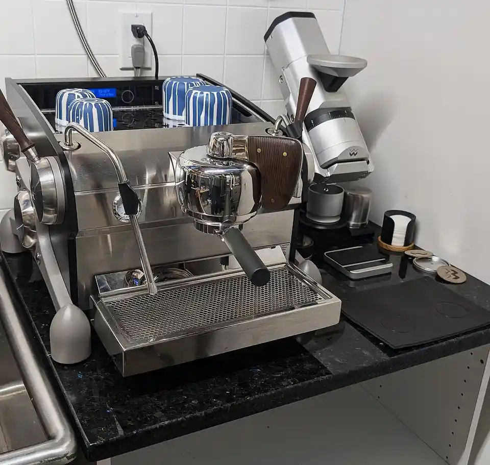 A stainless steel espresso machine sits on a black countertop, with three blue-and-white striped cups resembling R2-D2's…