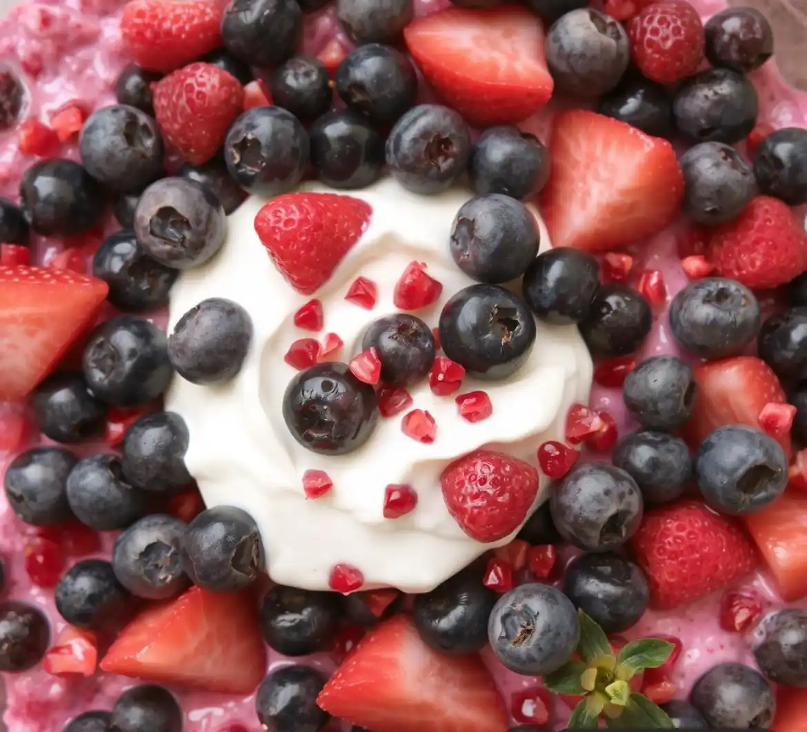 A close-up of a colorful yogurt bowl topped with fresh blueberries, sliced strawberries, and pomegranate seeds. The text…