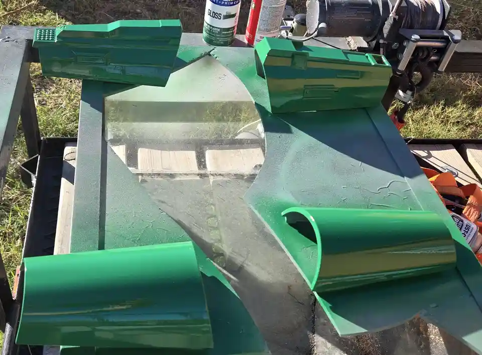 A freshly painted green tractor part, likely a front-end loader or similar attachment, is shown outdoors on a work surface…
