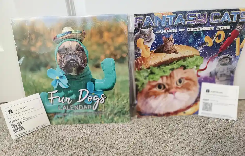Two 2025 wall calendars sit side-by-side on a carpet: one titled 'Fun Dogs' featuring a bulldog in a cactus costume with a…