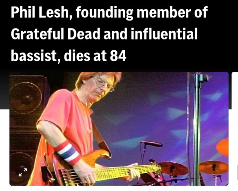 A photo of Phil Lesh, a man with glasses and reddish hair wearing a pink shirt and a red, white, and blue wristband, playing…