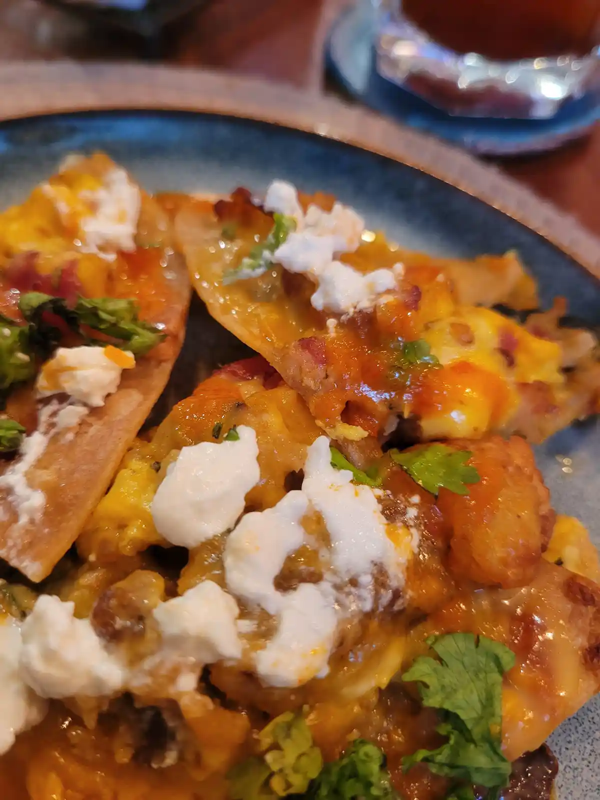 A close-up photo of a plate of cheesy, saucy, crispy-edged food topped with crumbled white cheese and fresh green herbs…