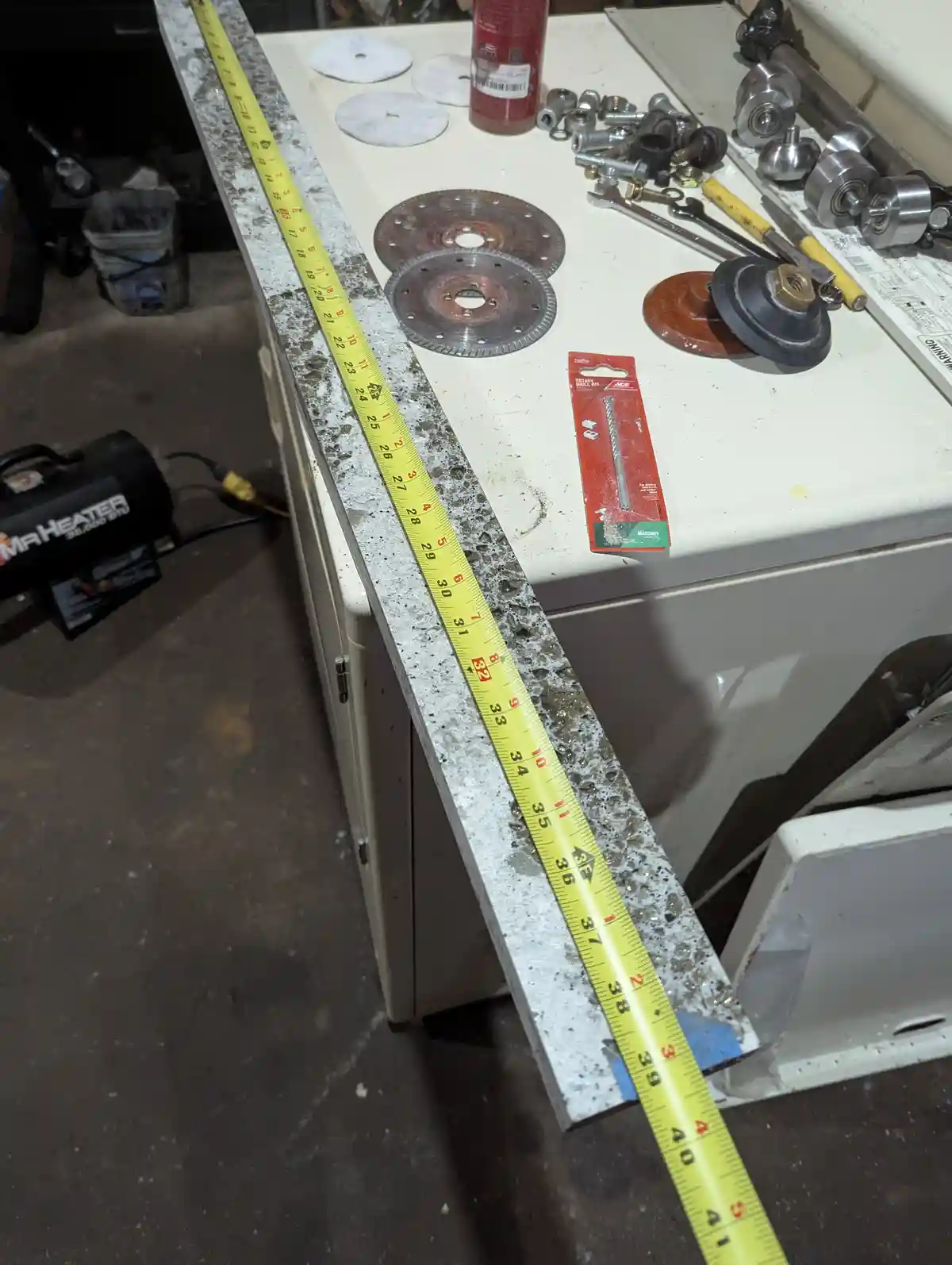A yellow measuring tape is stretched across a worn, speckled workbench surface, showing a measurement of 41 inches. The…