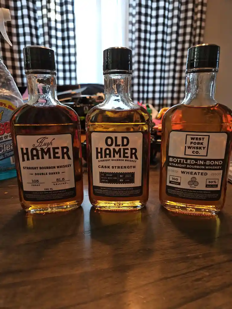 Three small bottles of bourbon whiskey labeled 'Hugh Hamer', 'Old Hamer', and 'West Fork Whisky Co.' sit side-by-side on a…
