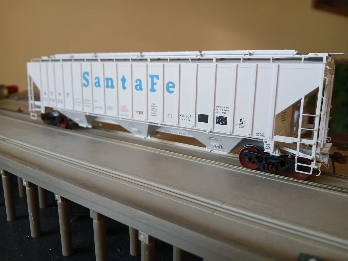 A detailed model of a white Santa Fe freight train car sits on a model railroad track, with blue 'Santa Fe' lettering…