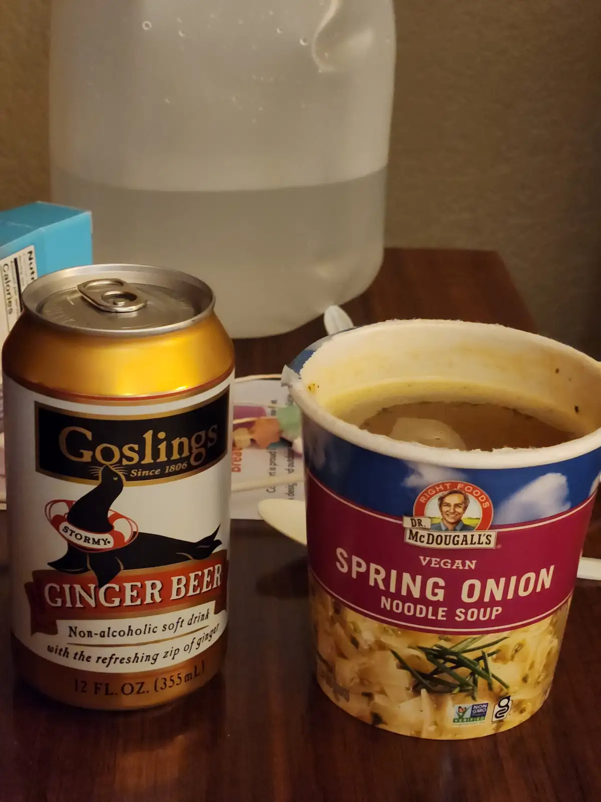 A can of Goslings Stormy Ginger Beer sits next to an open cup of Dr. McDougall's Vegan Spring Onion Noodle Soup on a wooden…