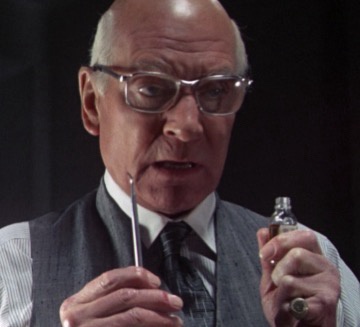 a close-up of a bald man with glasses, wearing a vest and tie, holding a small bottle and a dropper, looking intensely at…