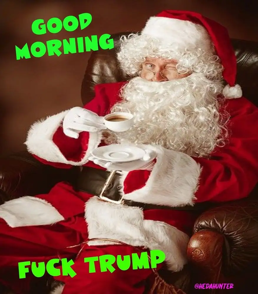 A man dressed as Santa Claus, wearing glasses and a red suit with white fur trim, sits in a brown leather armchair holding a…