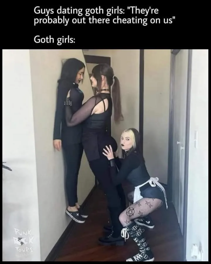 Three women dressed in goth fashion are in a hallway. One woman is standing against the wall, another is leaning against…