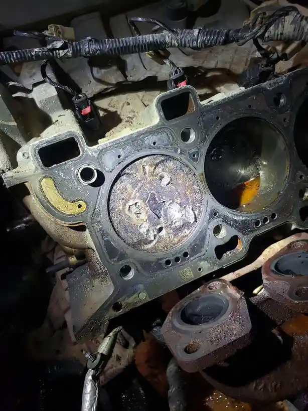 A close-up photo shows a severely damaged car engine block with melted, burnt, and corroded metal surfaces, surrounded by…