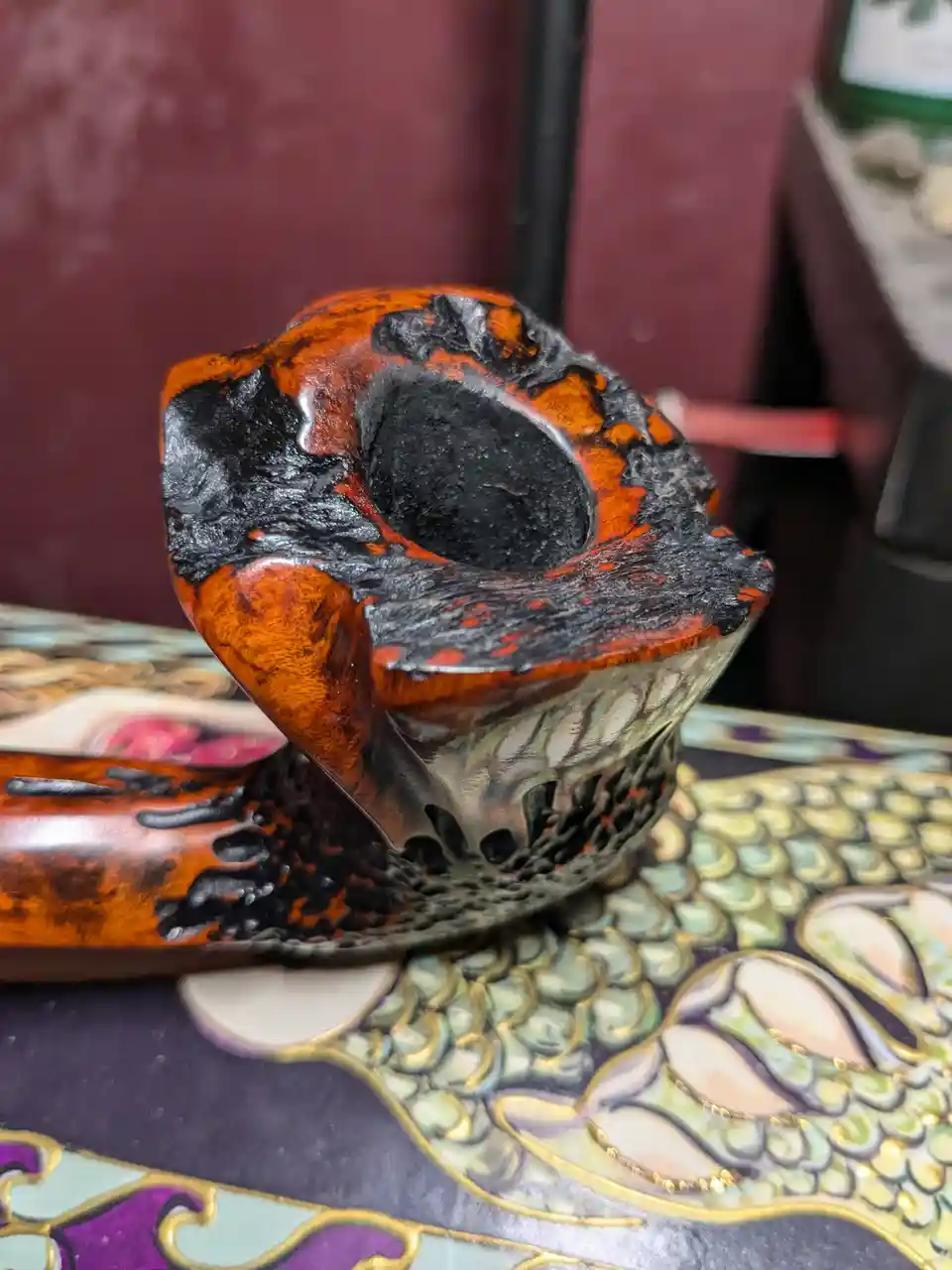 a close-up photo of a wooden smoking pipe with a heavily charred and blackened bowl, showing deep soot and burn marks that…