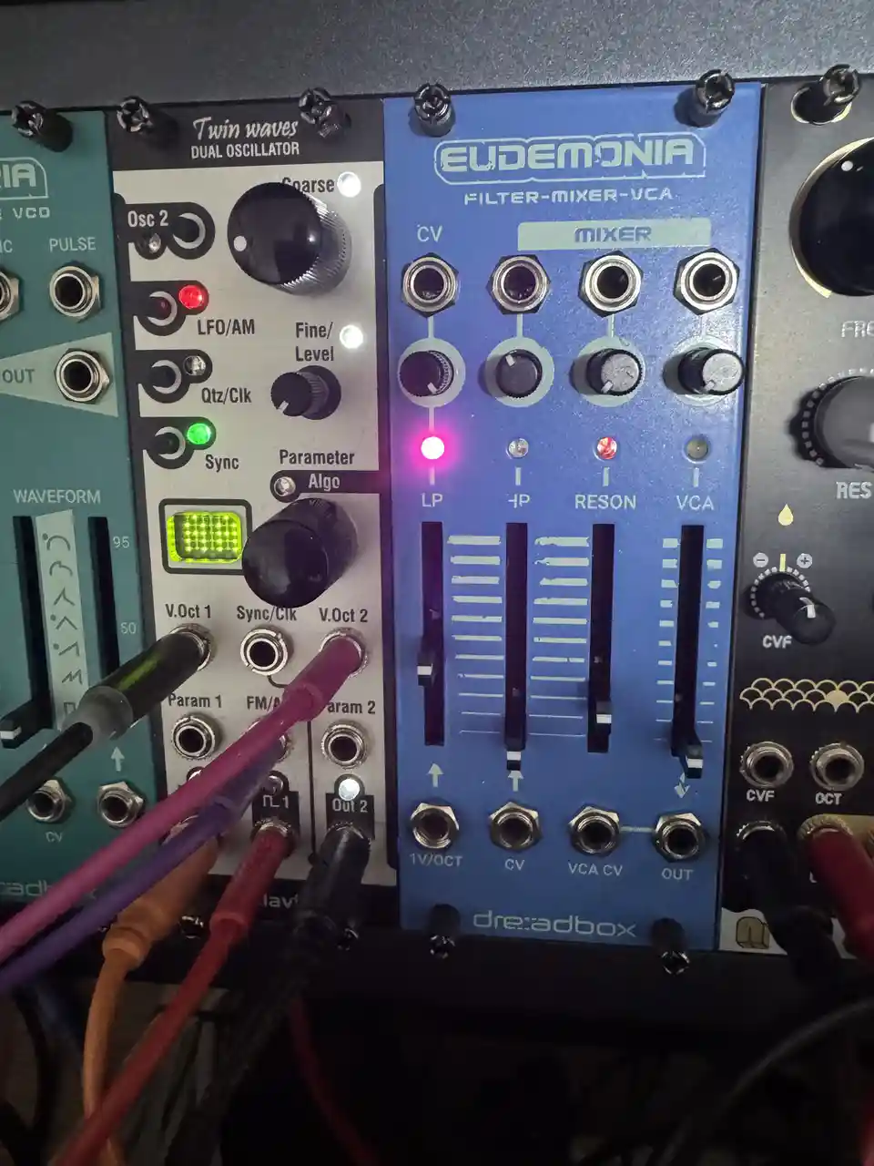 A close-up photo of a blue 'Eudemonia Filter-Mixer-VCA' module by dre:adbox, next to a 'Twin Waves Dual Oscillator' module…
