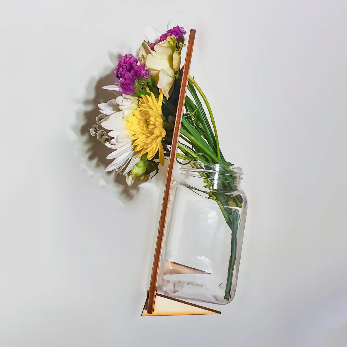 A clear glass jar filled with colorful flowers including yellow, white, and purple blooms is mounted on a minimalist…