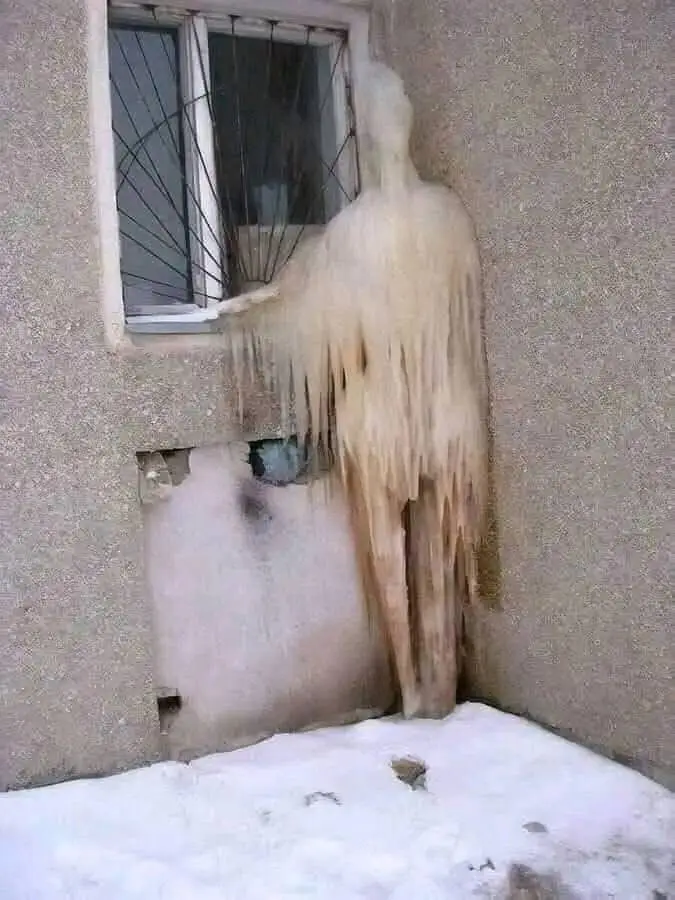 A tall, humanoid shape made of ice and frost stands against the corner of a building, appearing to be frozen in place next…