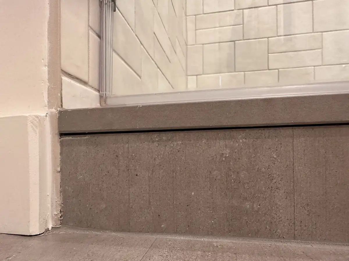 A close-up photo shows the bottom of a shower stall with a visible gap between the shower base and the surrounding floor…