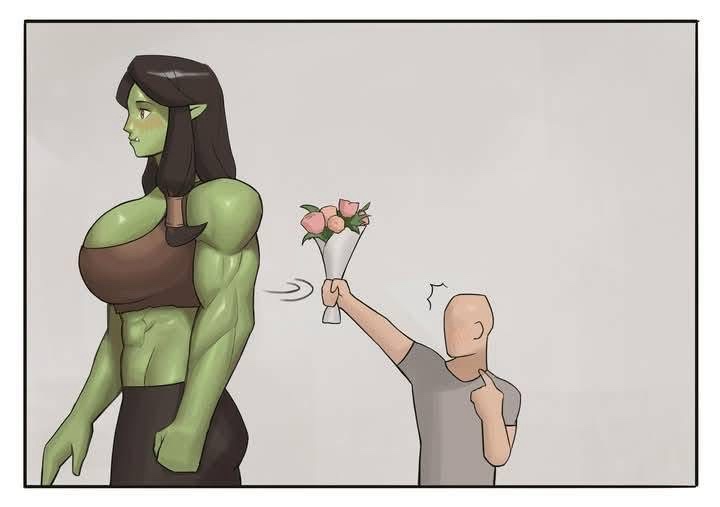 A muscular green-skinned woman with long dark hair stands facing away from a bald man in a grey t-shirt. The man is holding…