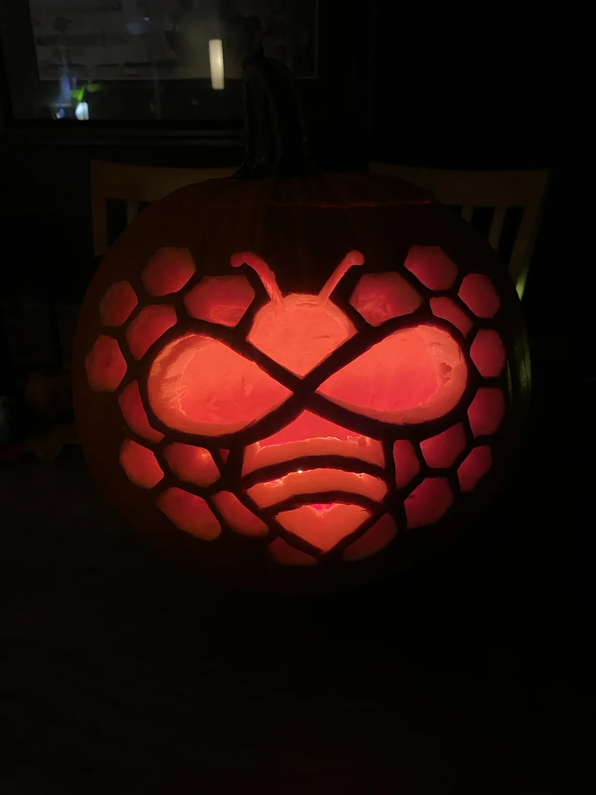 A carved Halloween pumpkin with a glowing red interior, featuring a face with large round eyes, a wide mouth, and antennae…
