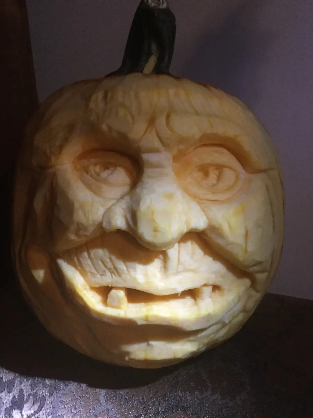A close-up of a highly detailed, intricately carved pumpkin with a realistic human-like face, featuring deep-set eyes, a…