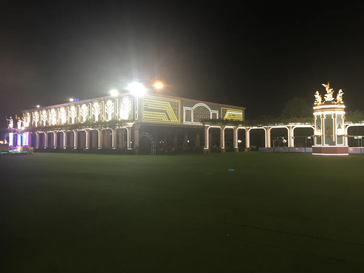 A grand, ornate building is illuminated at night with bright yellow and white lights outlining its architectural features…