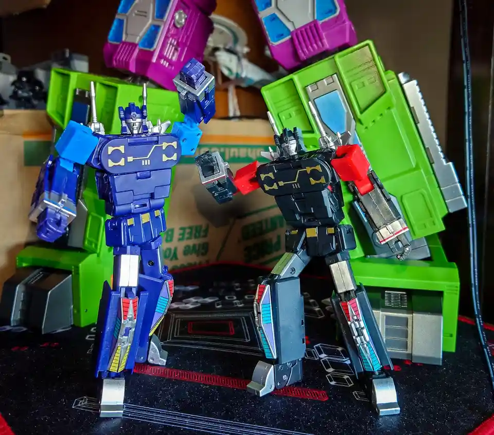 Two Transformers action figures, one blue and one black, stand facing each other in a confrontational pose on a black…