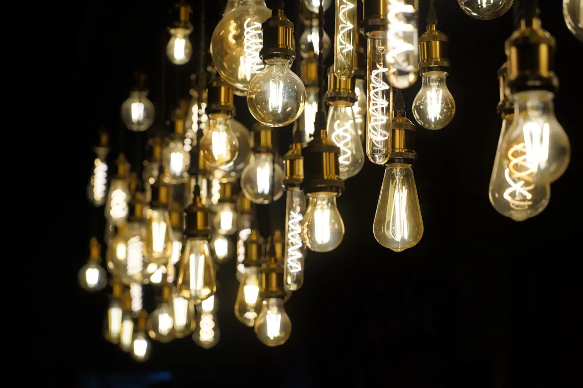A close-up photo of numerous glowing, vintage-style Edison bulbs hanging in a cluster against a dark background. The bulbs…