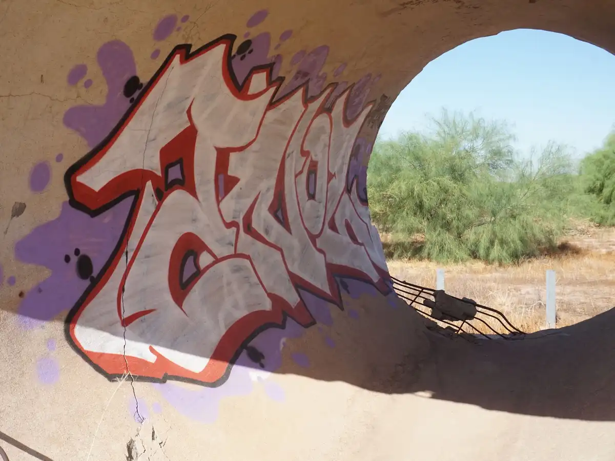A photo of graffiti on a curved concrete wall under a bridge, showing the word 'zack' in stylized white letters with red and…