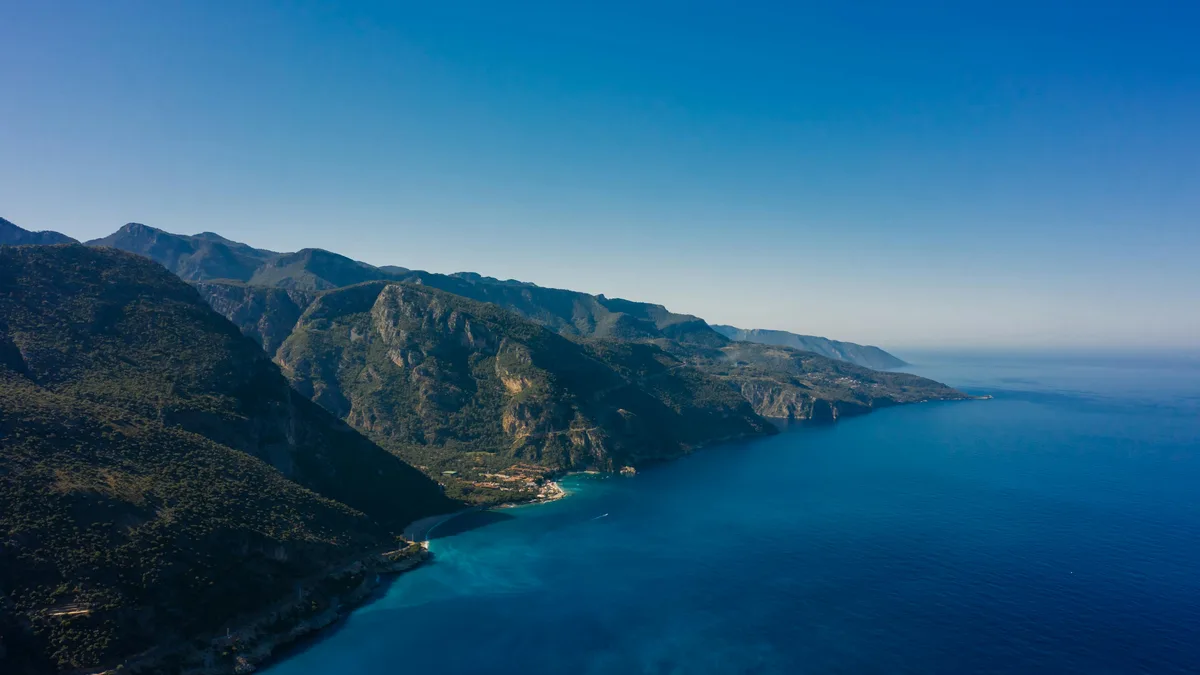 Towering mountains plunge into the crystal-clear turquoise sea, their rugged peaks reaching for the brilliant blue sky…