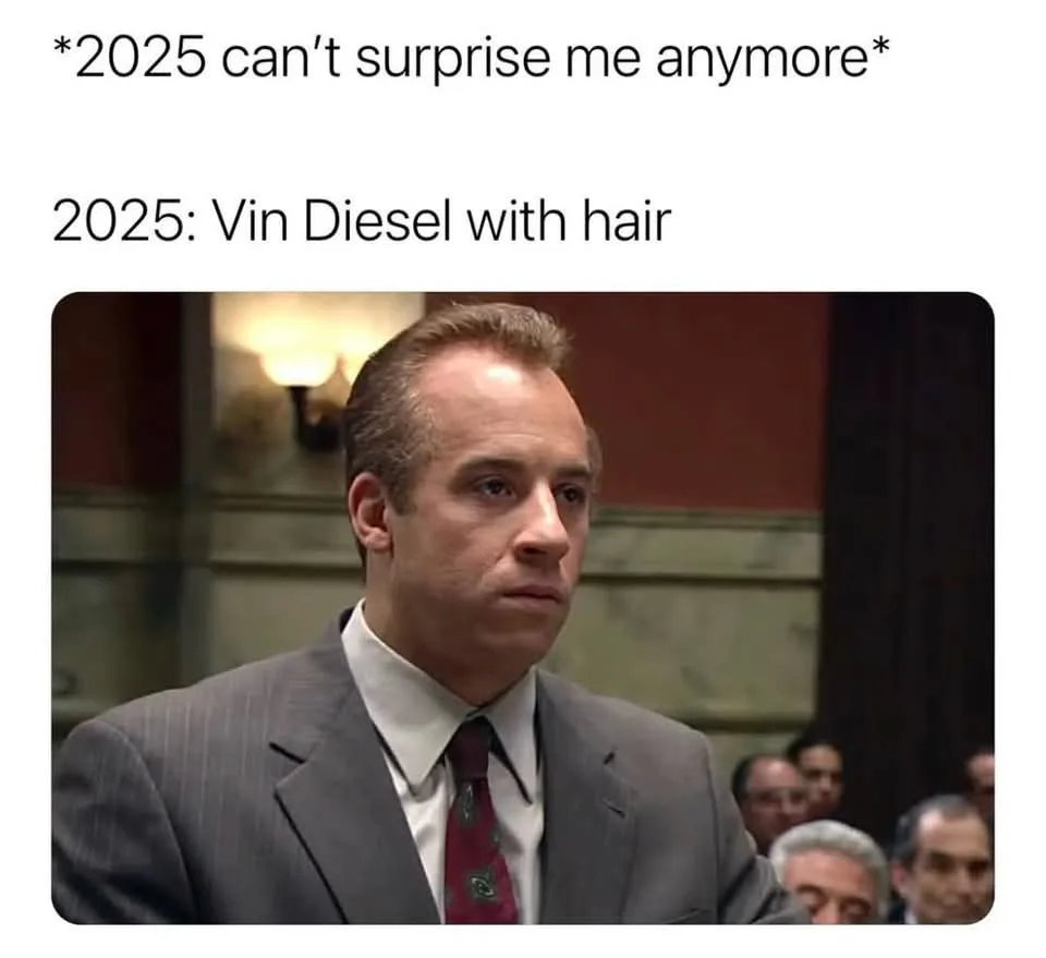 A still image of actor Vin Diesel in a pinstripe suit and red tie, looking slightly bewildered or resigned. The overlaid…