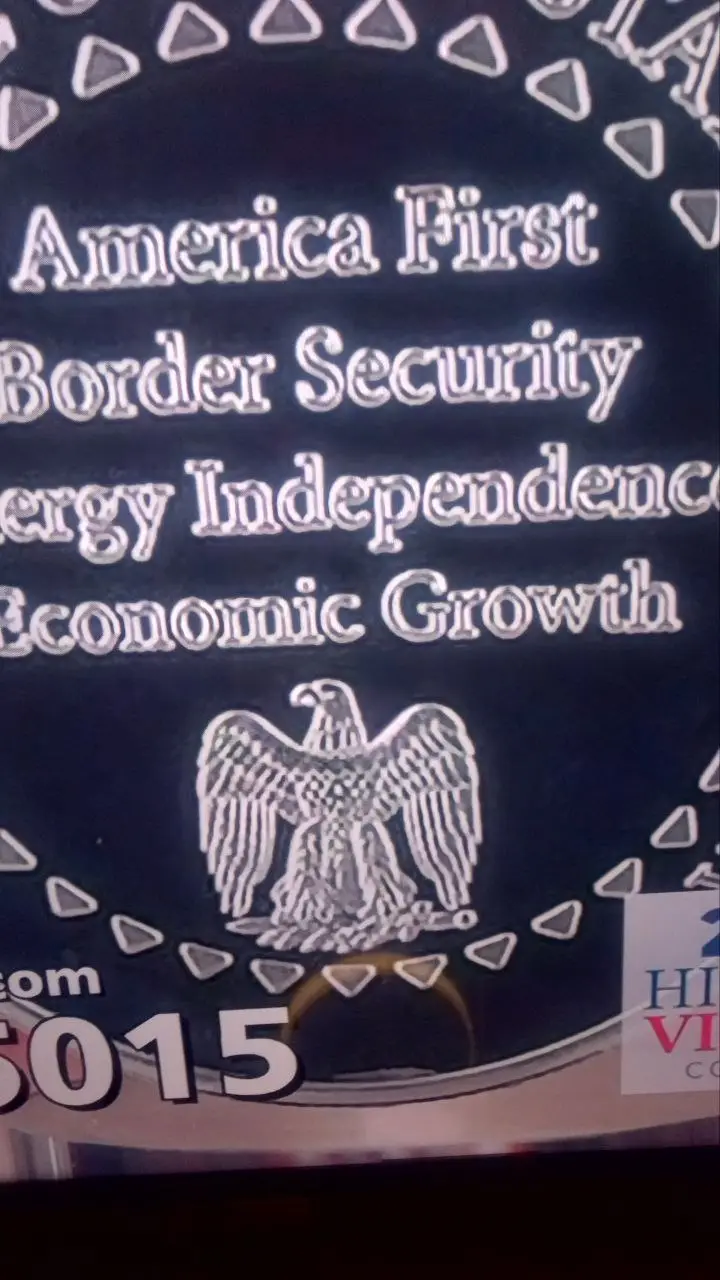 A close-up of a dark blue circular seal featuring a silver embossed eagle and text listing policy priorities: 'America…