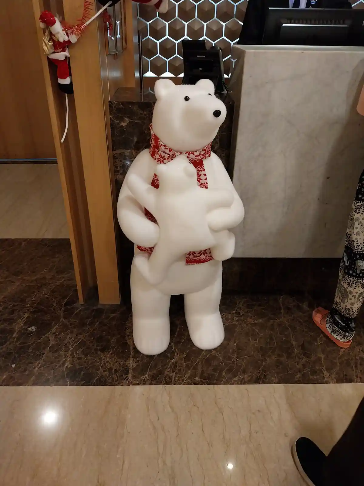 A large white polar bear statue wearing a red and white patterned scarf is holding a smaller polar bear statue in its arms…