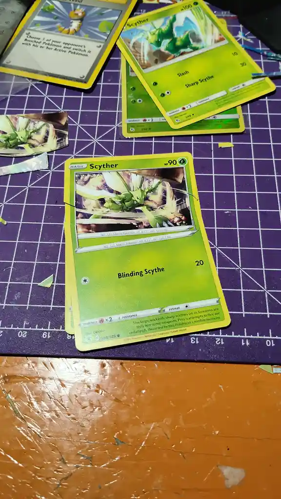 A close-up photo shows a damaged Pokémon Trading Card Game card of Scyther, with its artwork partially torn and the text…