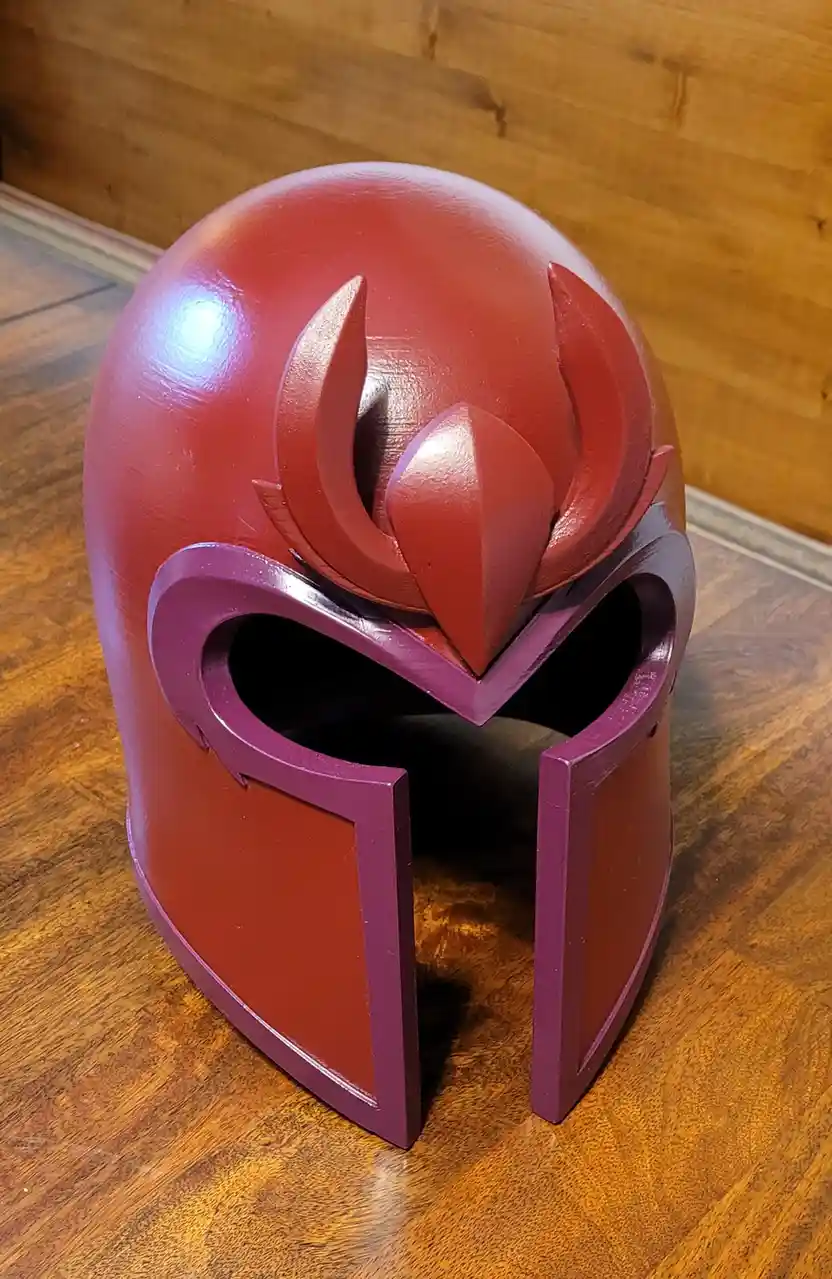 A red and purple helmet with a stylized flame-like crest sits on a wooden floor against a wooden wall. The overlaid text…