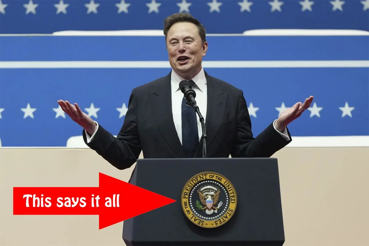 A man in a dark suit and tie stands behind a podium bearing the Seal of the President of the United States, gesturing with…