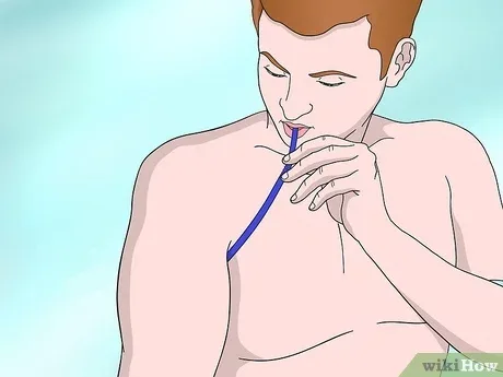 A shirtless man with reddish hair is shown blowing a bubble with a blue bubble wand, eyes closed in concentration. The image…